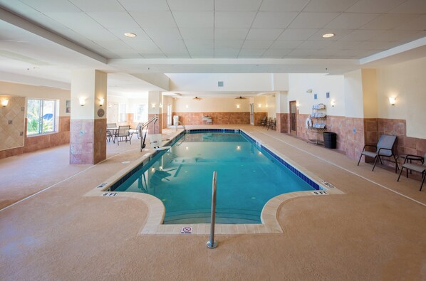 Una piscina interior con un cartel de prohibición de saltos, rodeada de sillas de descanso y una pared de azulejos.
