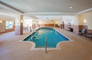An indoor swimming pool with a no diving sign, surrounded by lounge chairs and a tiled wall.