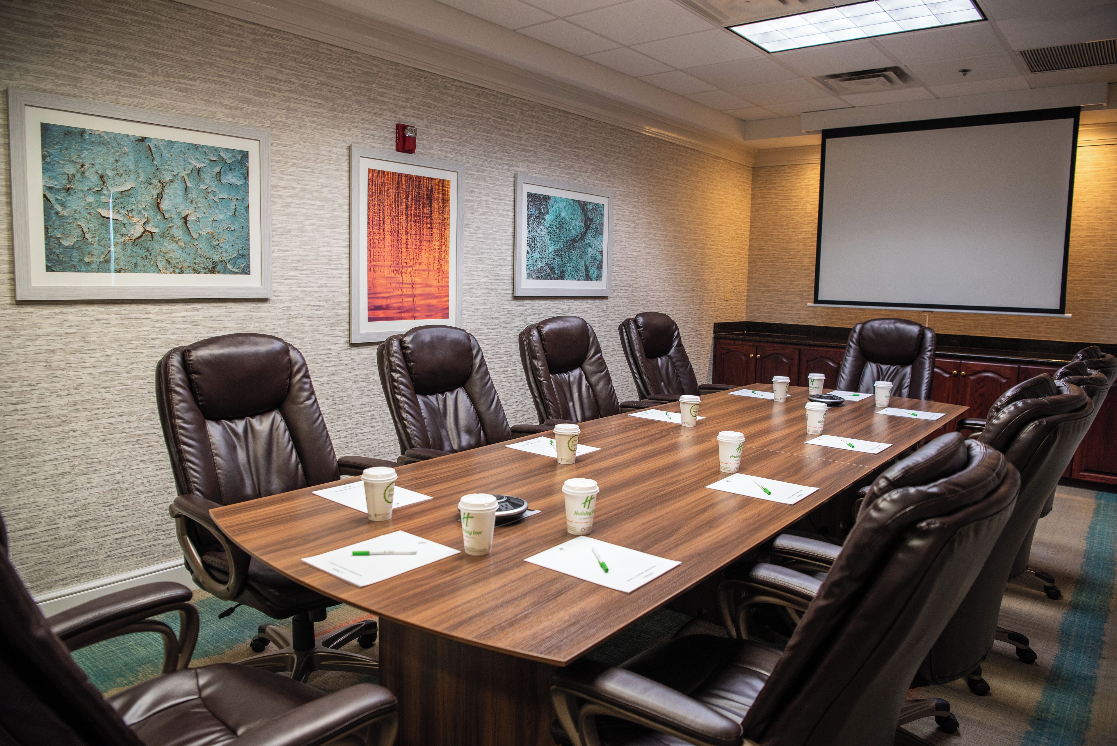 A conference room with a long table, leather chairs, and framed artwork on the walls.