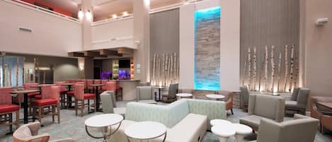 A spacious lobby with multiple seating areas, a bar, and a large window with a view.