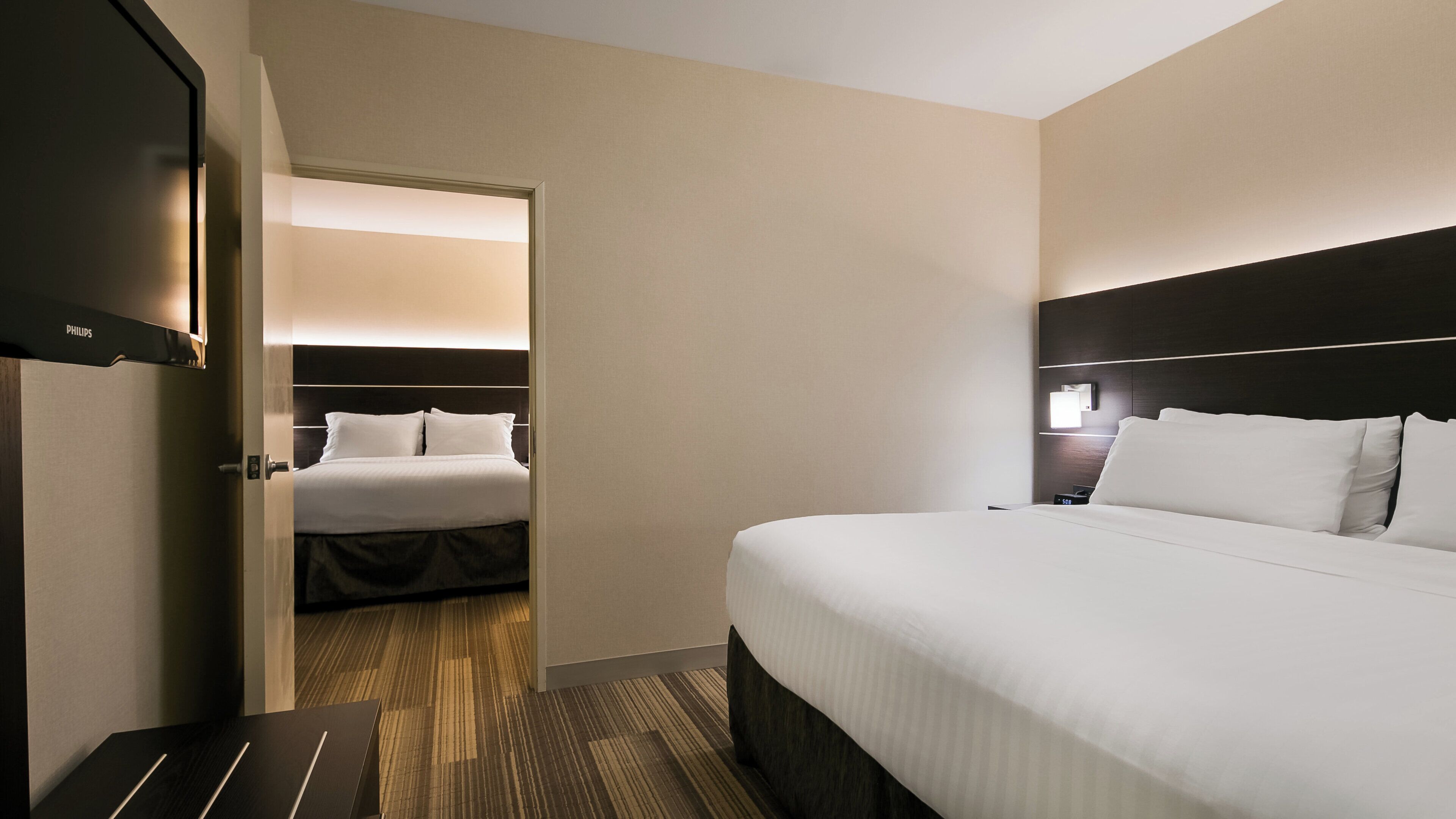 A hotel room with a bed, a bedside table, a nightstand, and a wall-mounted lamp.
