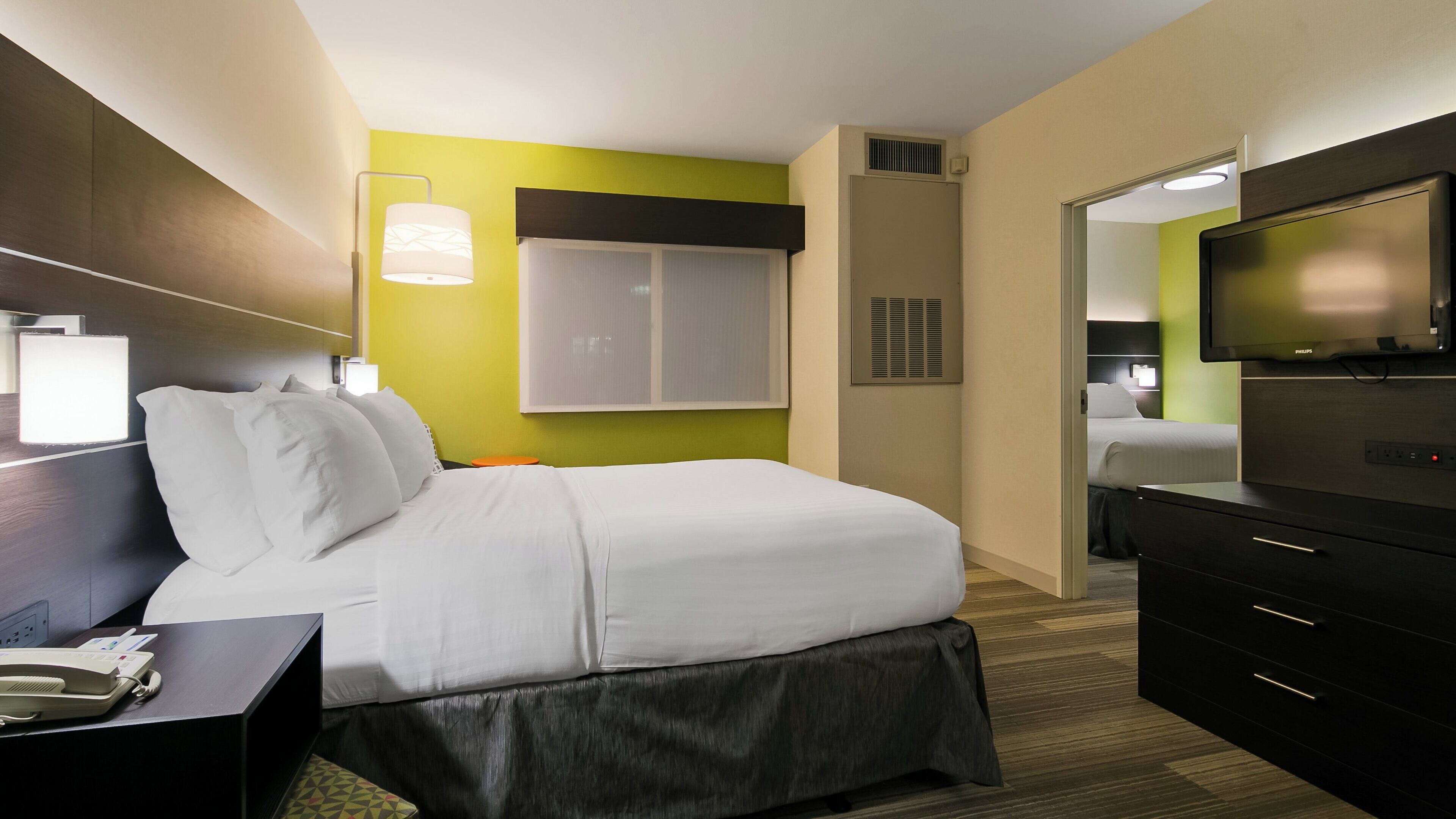 Ein Hotelzimmer mit Bett, Nachttisch, Lampe, Fernseher und Spiegel.