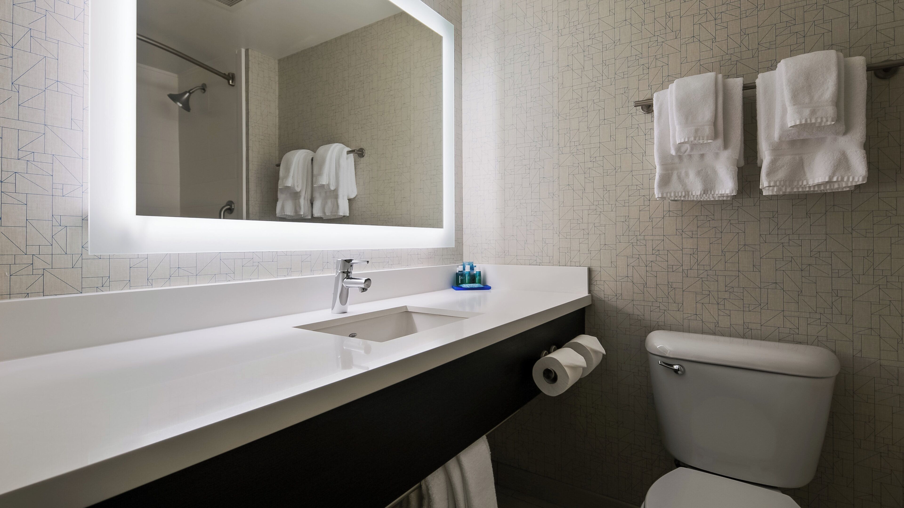 Et moderne badeværelse med en hvid vask, et spejl, et toilet og en håndklædestang med håndklæder.