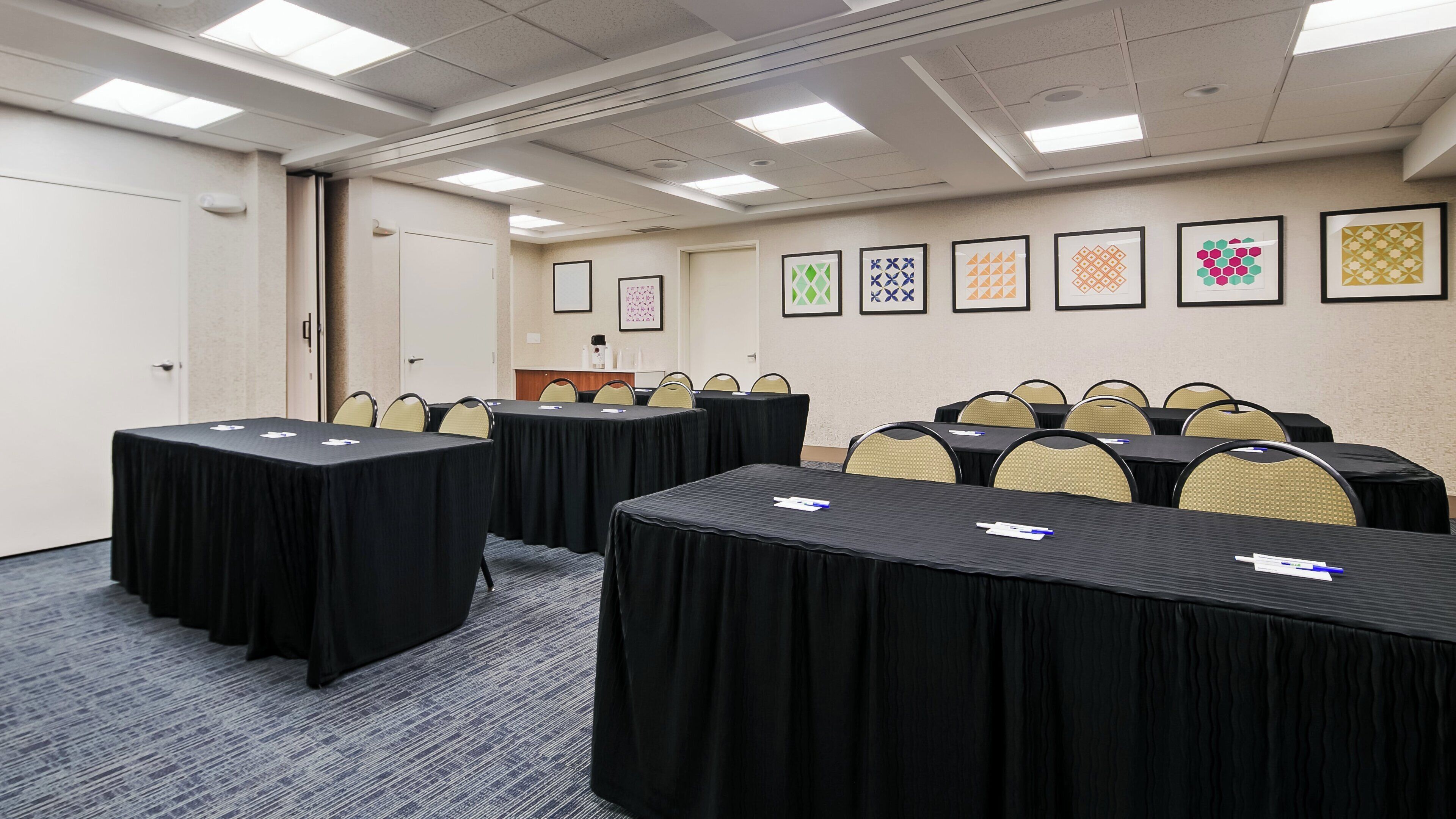 Un salón de conferencias con mesas y sillas, una puerta y cuadros en la pared.