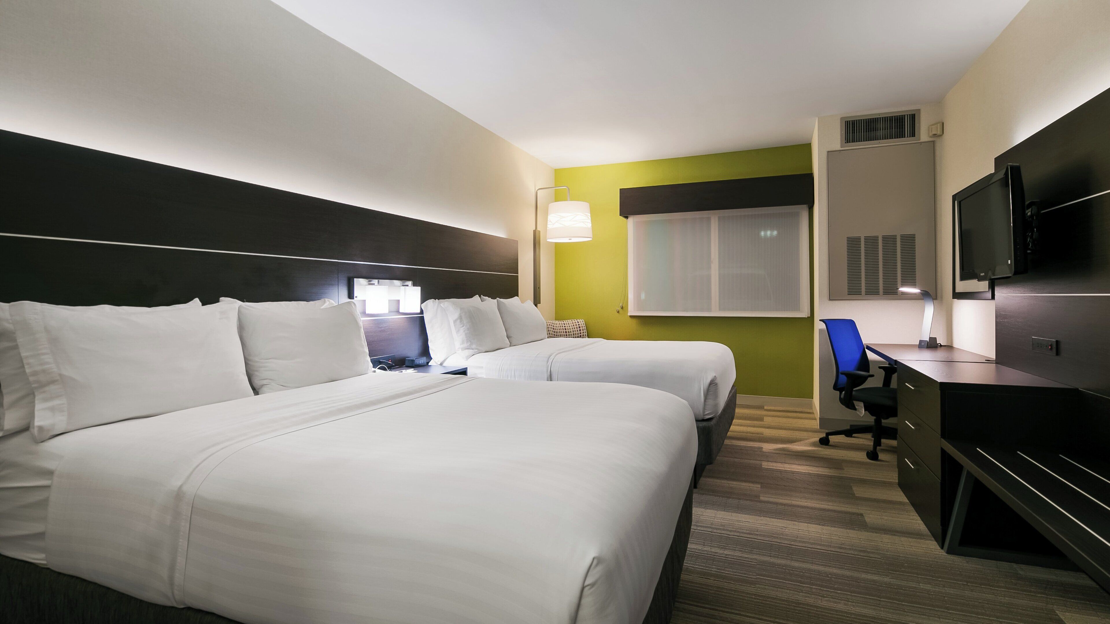 A hotel room with two beds, a desk, a chair, a television, and a window.
