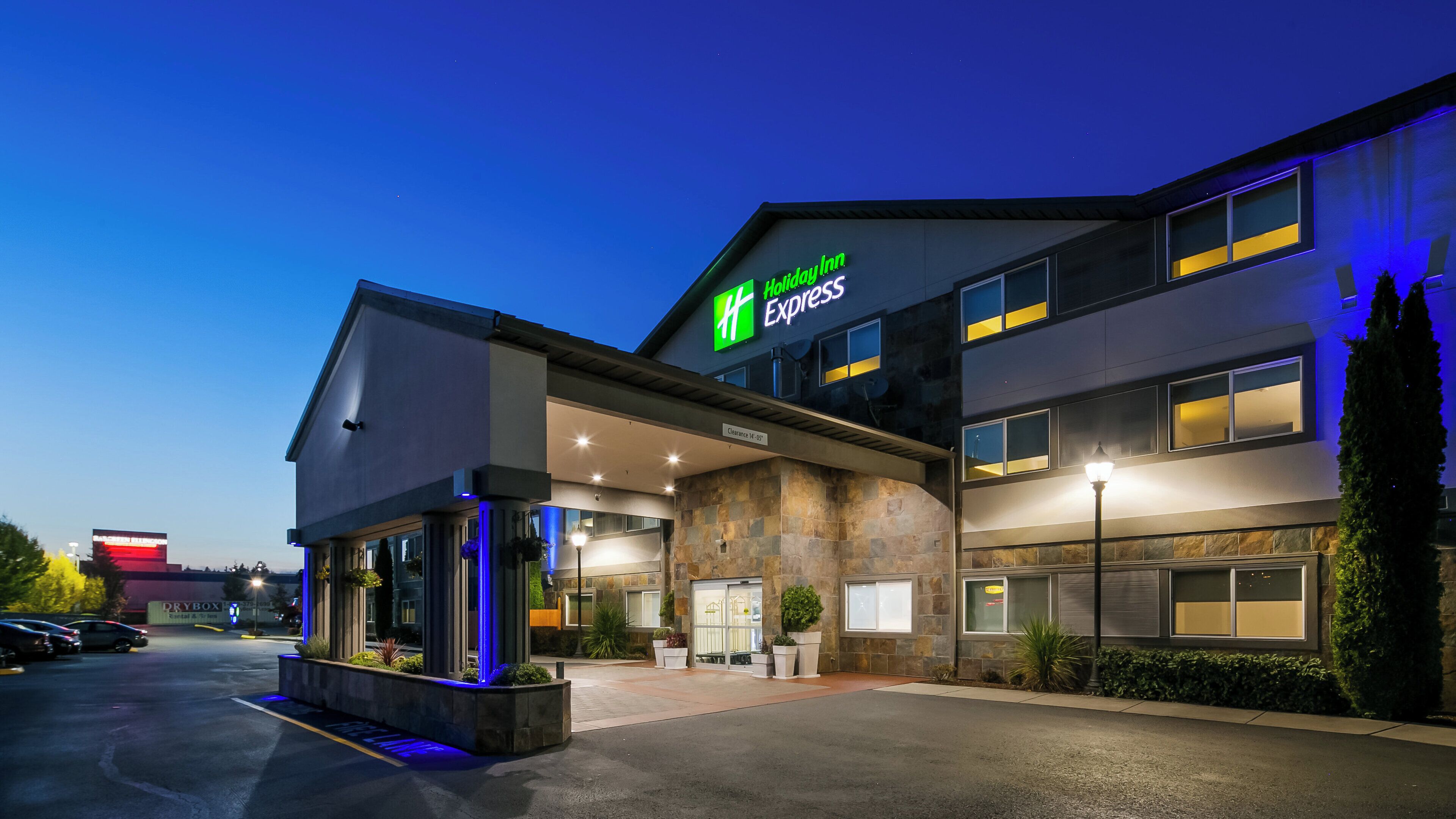 Un bâtiment de l’hôtel Holiday Inn Express avec une entrée bien visible, un parking et un panneau indiquant la hauteur maximale autorisée pour les véhicules.