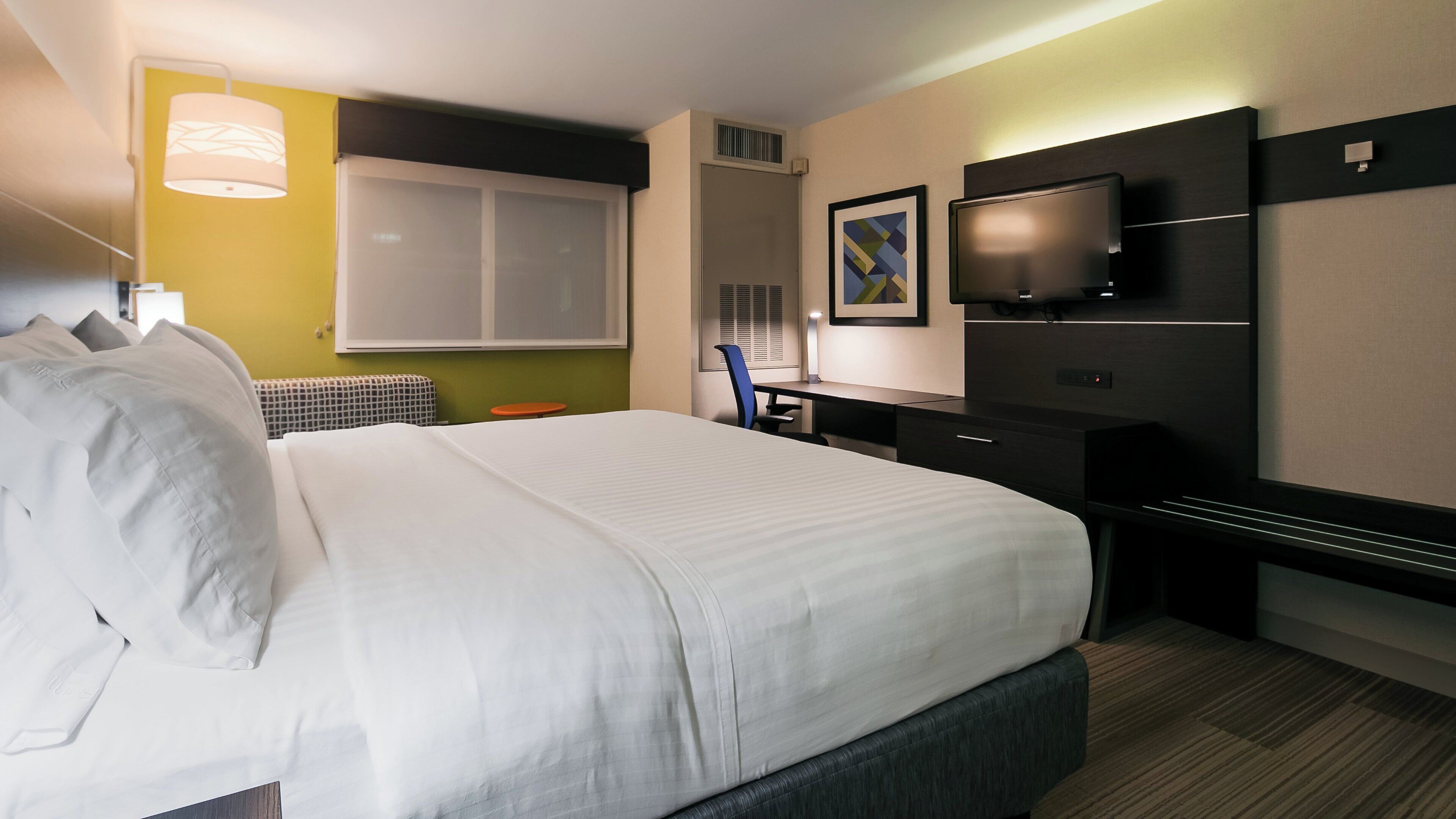 A hotel room with a large bed, a desk, a chair, a television, and a window.