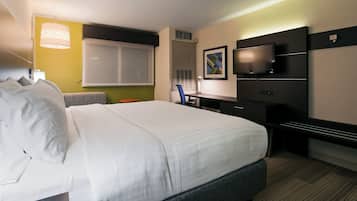 A hotel room with a large bed, a desk, a chair, a television, and a window.