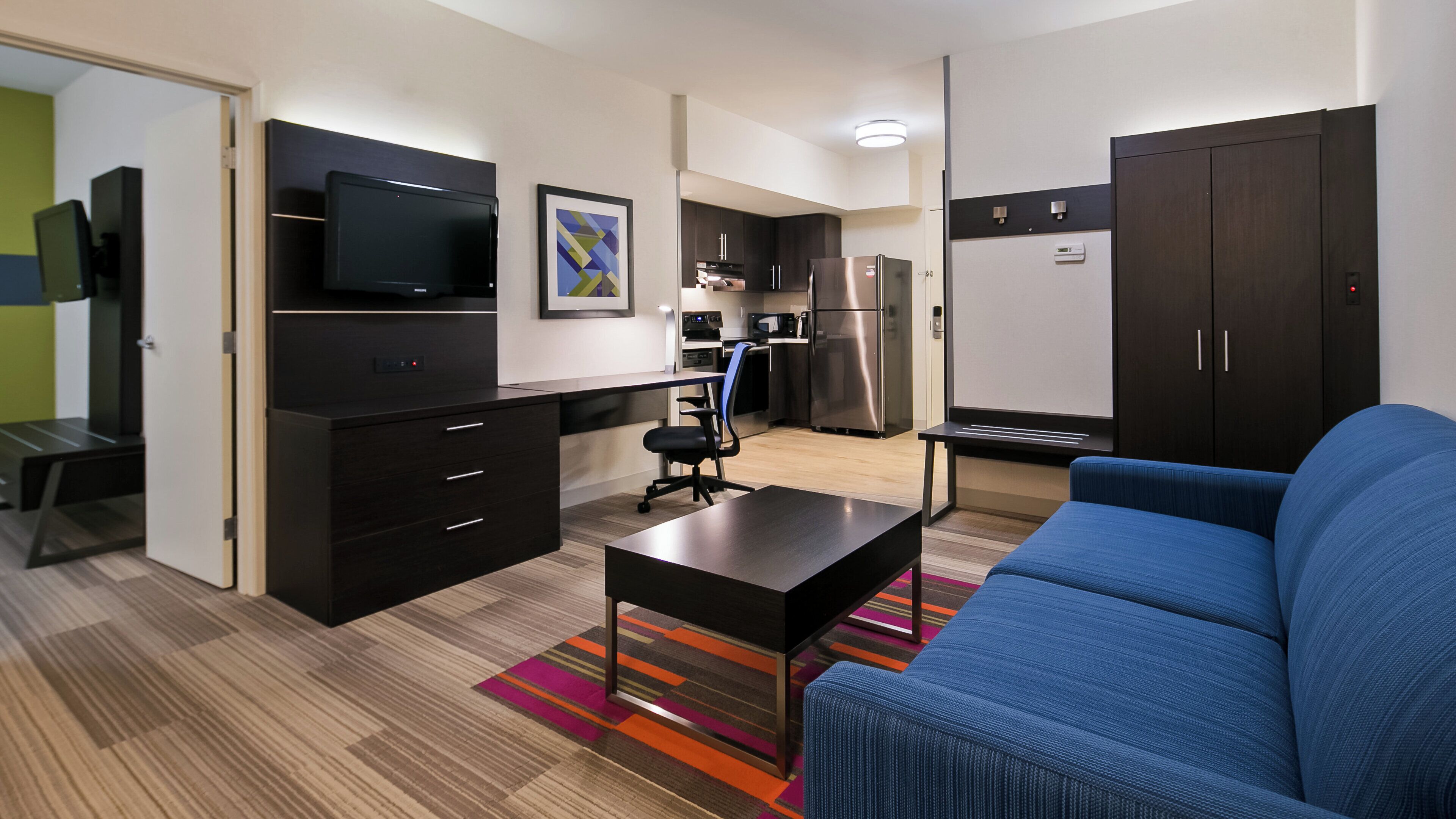 A compact living space with a kitchenette, a flat-screen TV, a sofa, and a small dining table.