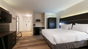 Quarto de hotel moderno com uma cama grande, uma escrivaninha, uma televisão de tela plana, micro-ondas e um guarda-roupa.