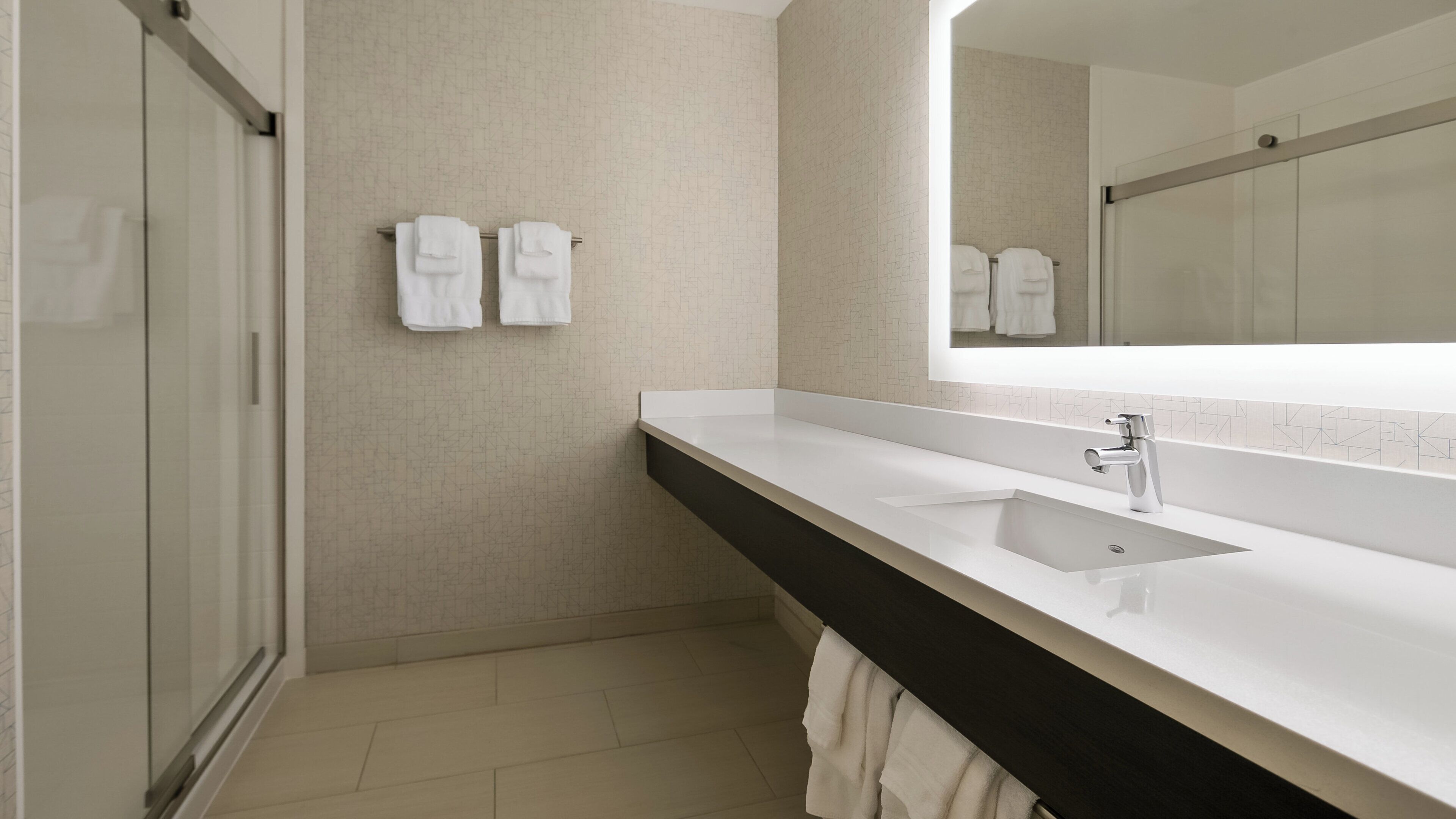 A modern bathroom with a large mirror, a sink, and two towels hanging on the wall.