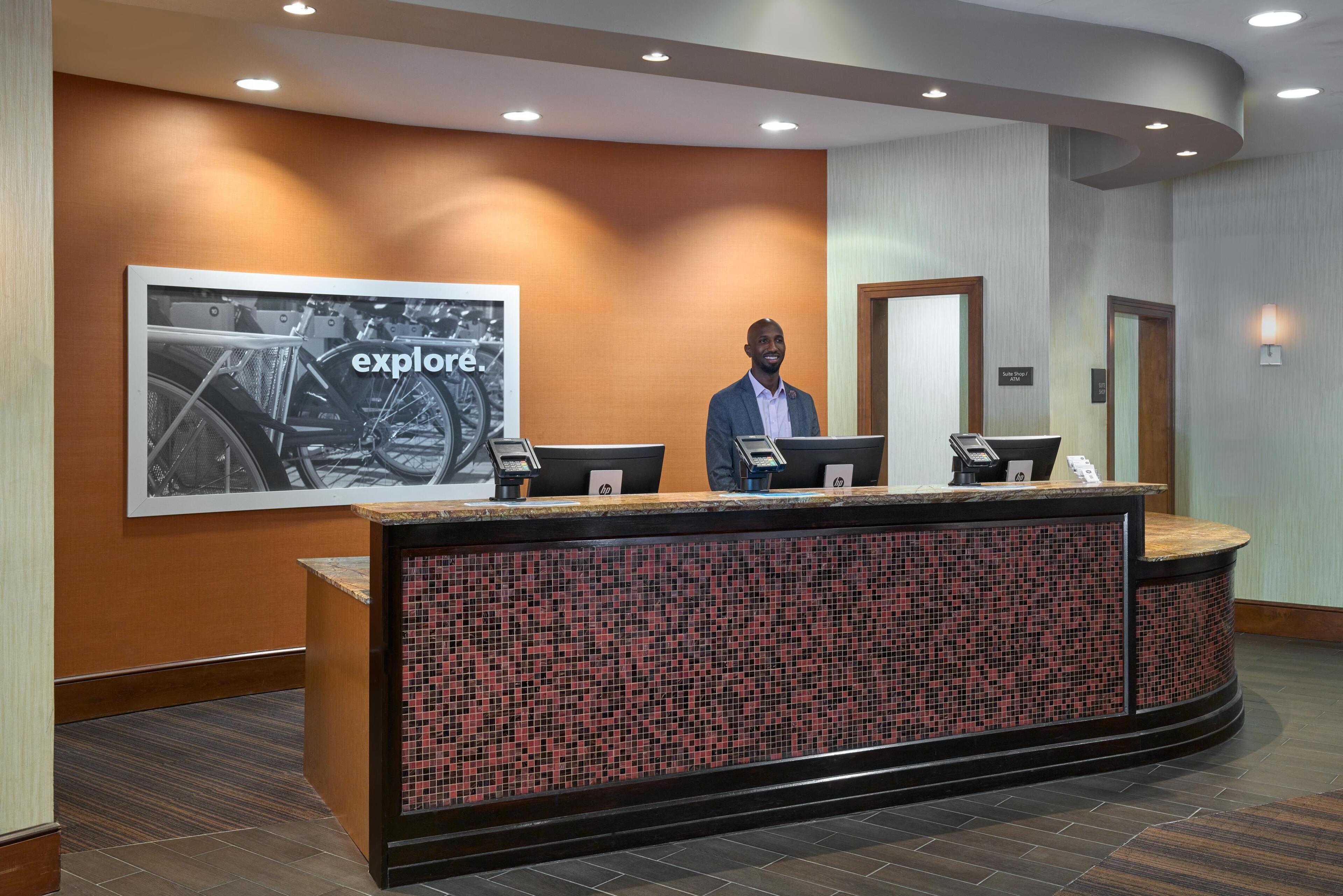 A reception desk with a tiled mosaic design, a framed 'explore' poster, and a sign indicating 'South Lobby'.