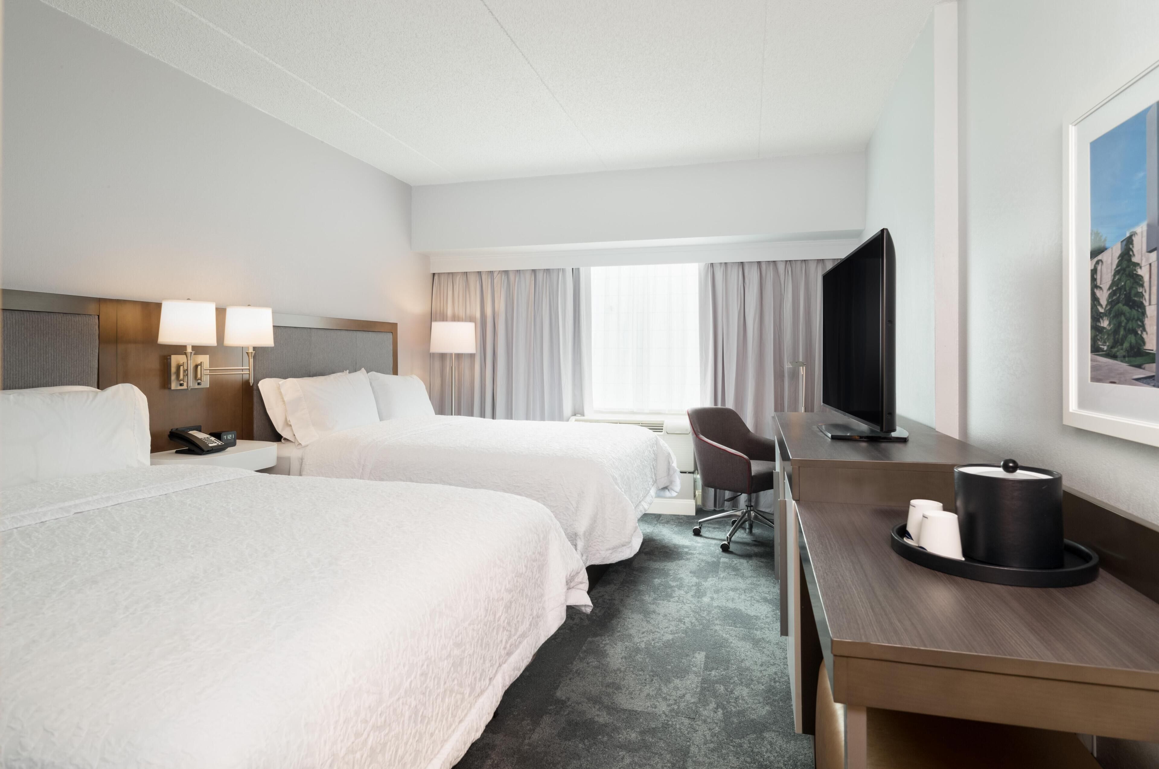 Habitación de hotel con dos camas, un escritorio, una silla, un televisor y un cuadro en la pared.
