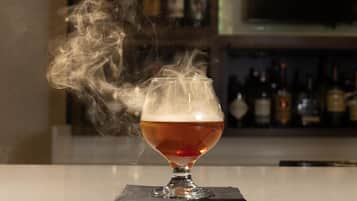 Un vaso de líquido color ámbar con espuma, que emite vapor, sobre un posavasos de bar.