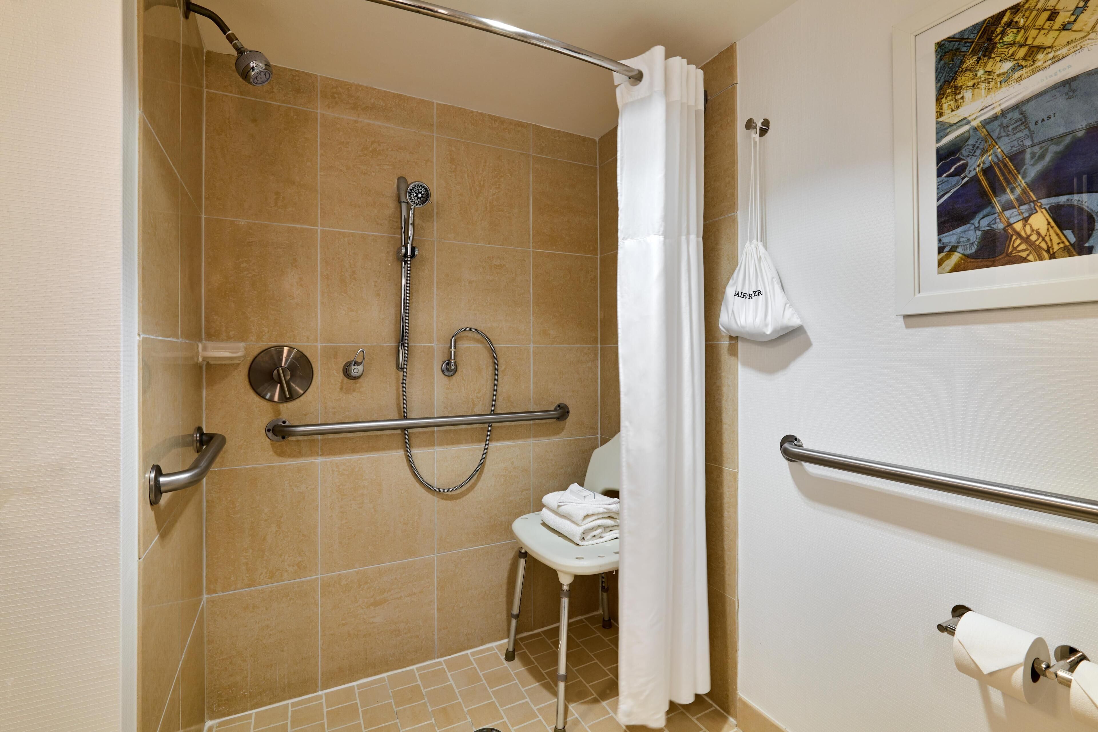 A bathroom with a shower, grab bars, a toilet, and a towel rack.