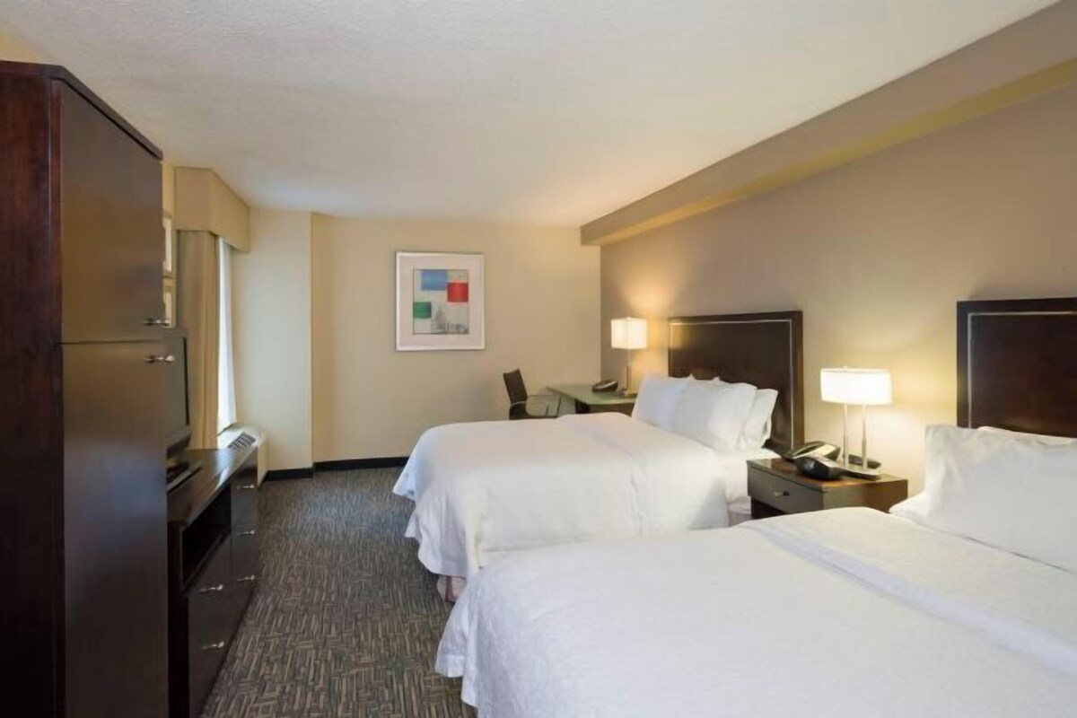 A hotel room with two beds, a desk, a chair, and a TV.