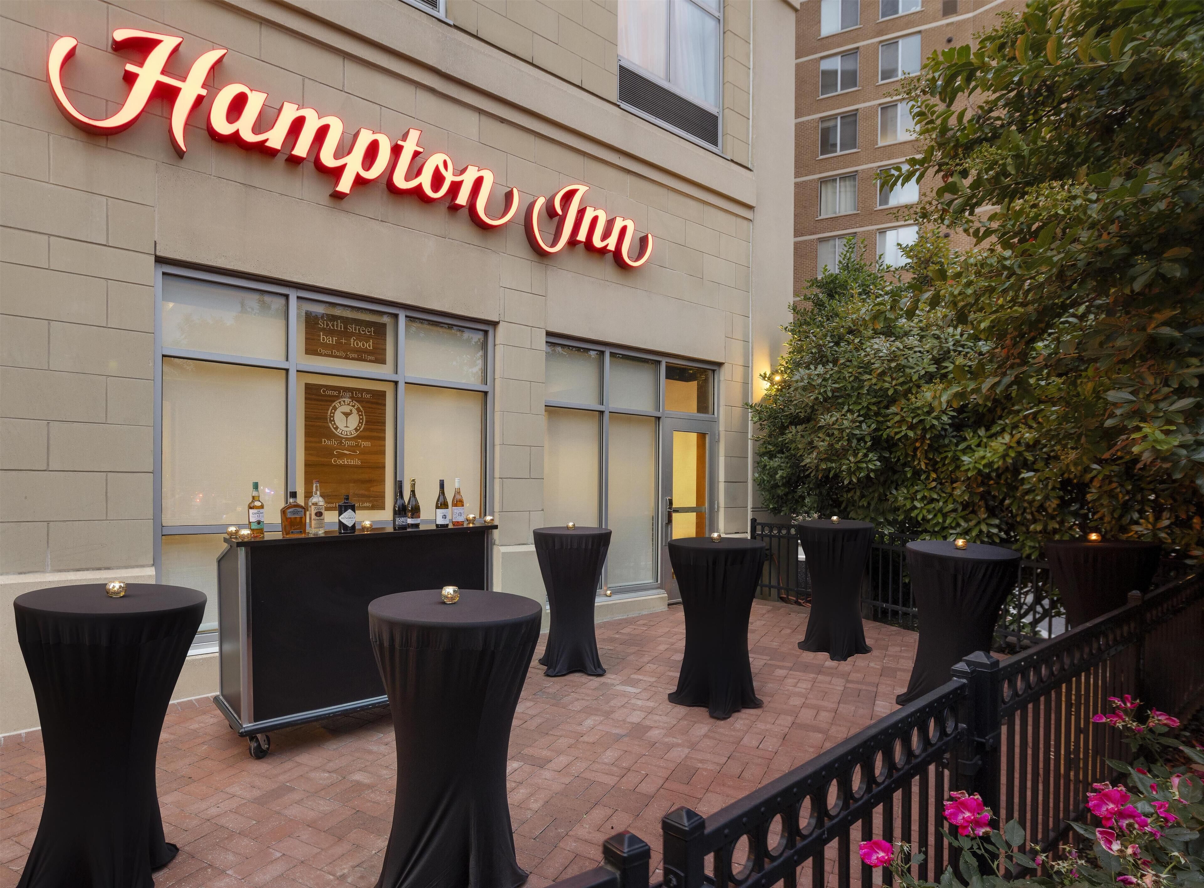 L’extérieur d’un hôtel Hampton Inn, avec un bar, des espaces de détente en plein air et une façade en briques.