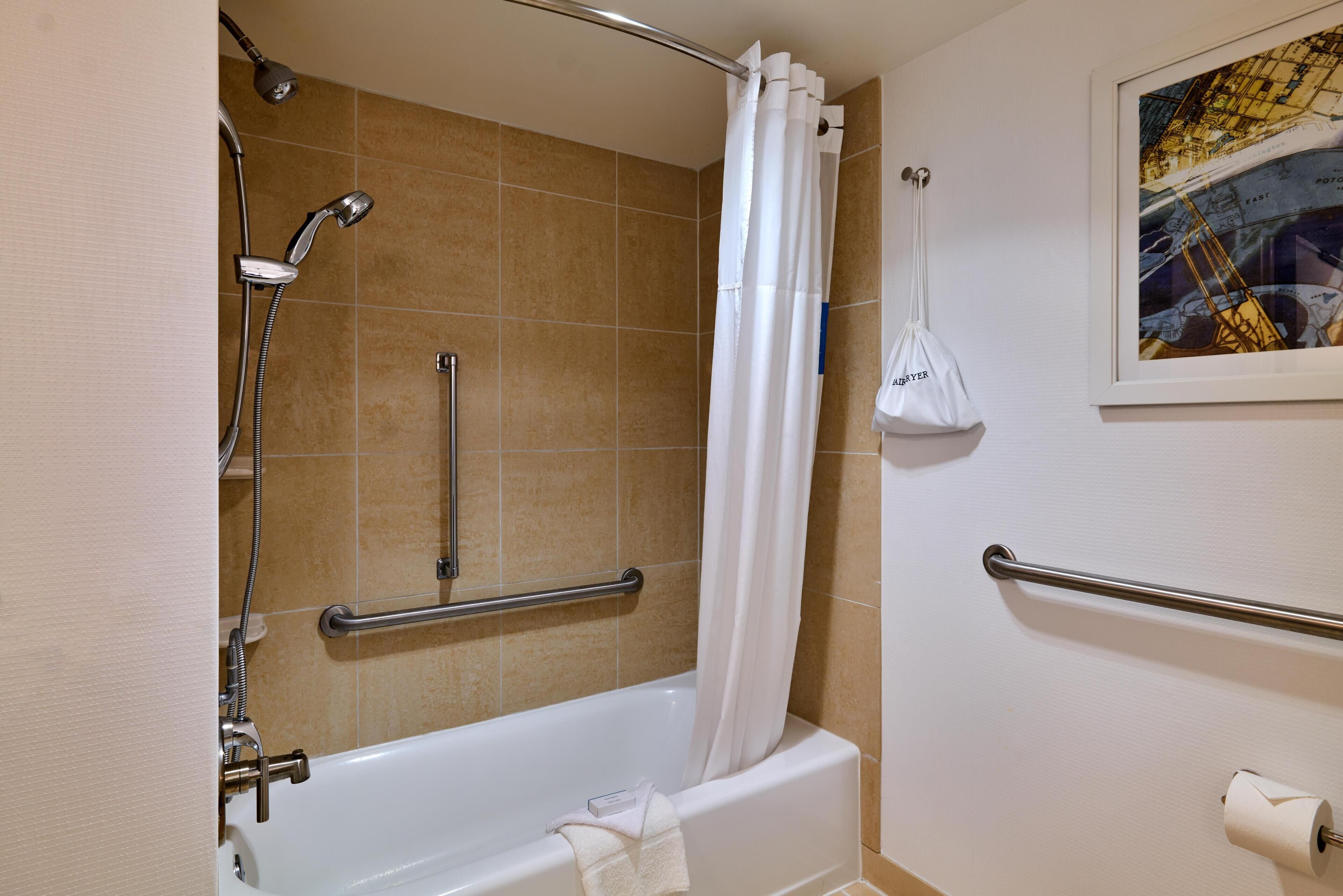 Een badkamer met een badkuip, douche, handgrepen, een handdoek en een inlijsting kaart aan de muur.