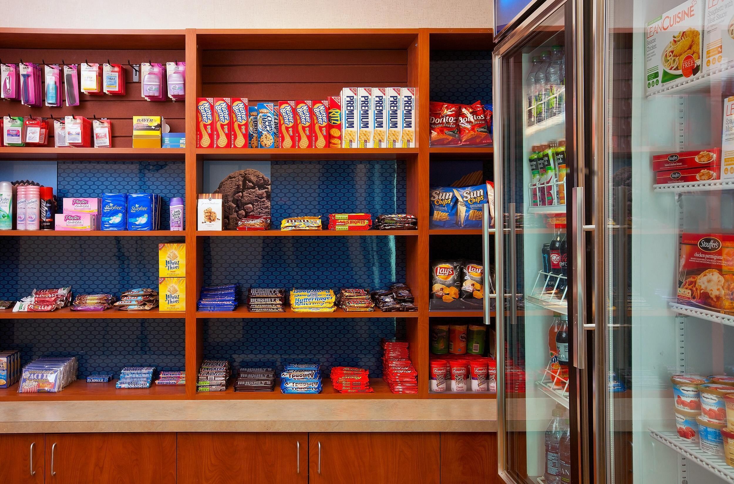 Un expositor de aperitivos con diversos productos envasados, un refrigerador con bebidas y una pared azul con diseño.