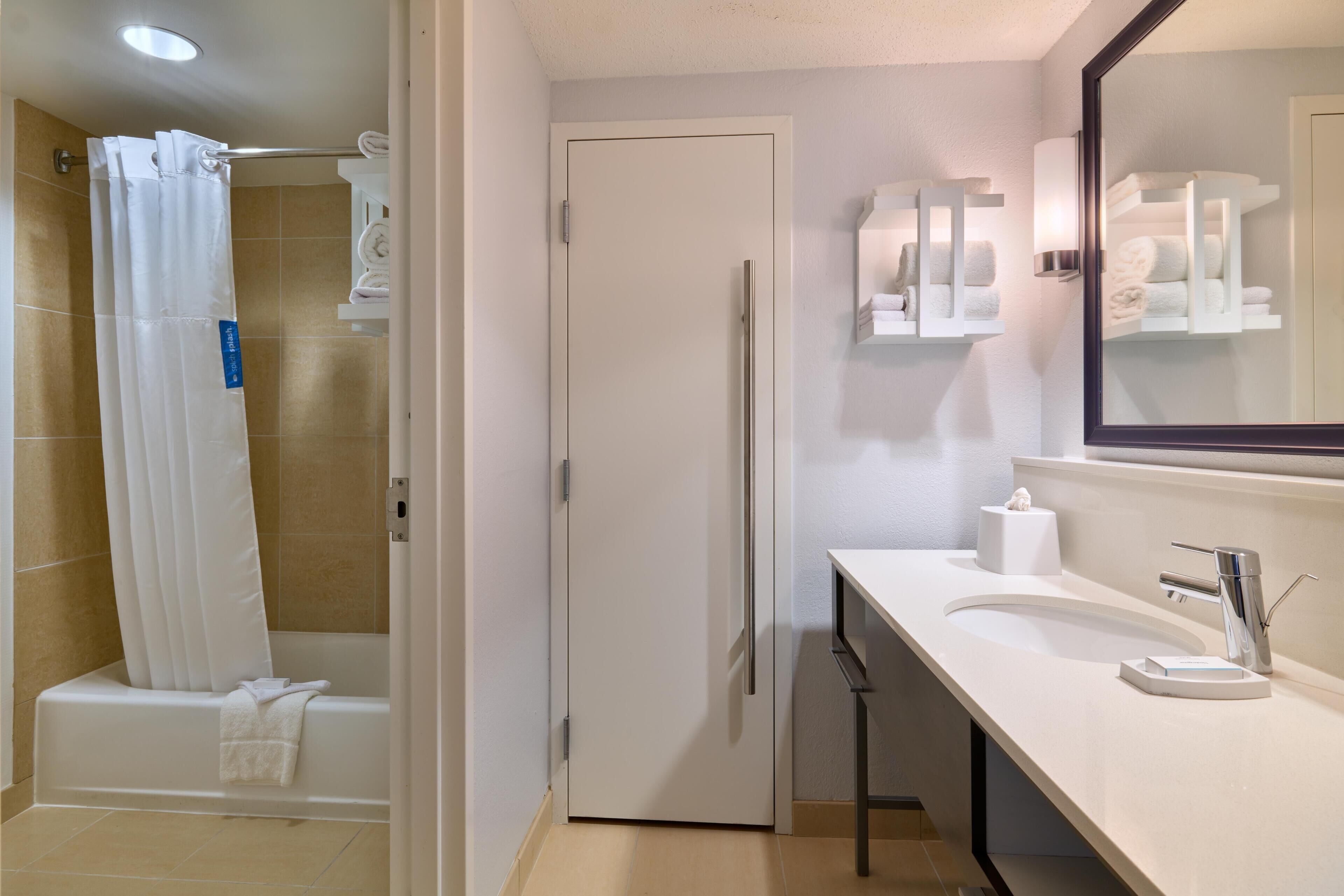 A bathroom with a shower, toilet, sink, and towel storage.