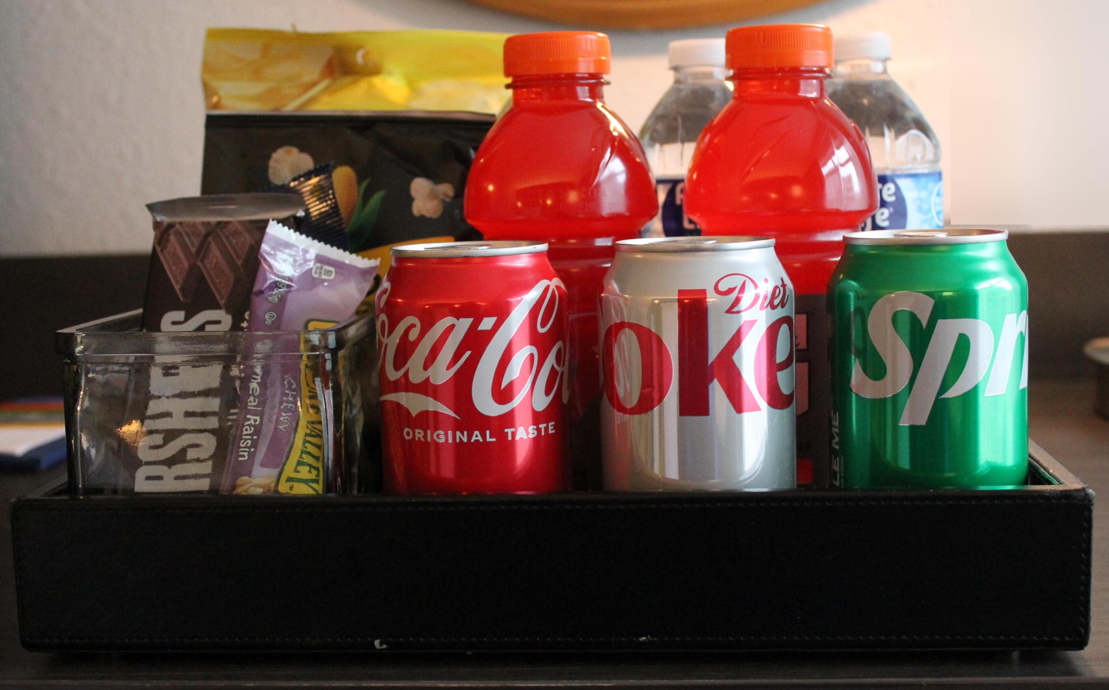 Bandeja con latas de Coca-Cola, Diet Coke y Sprite, y un vaso con bebida.