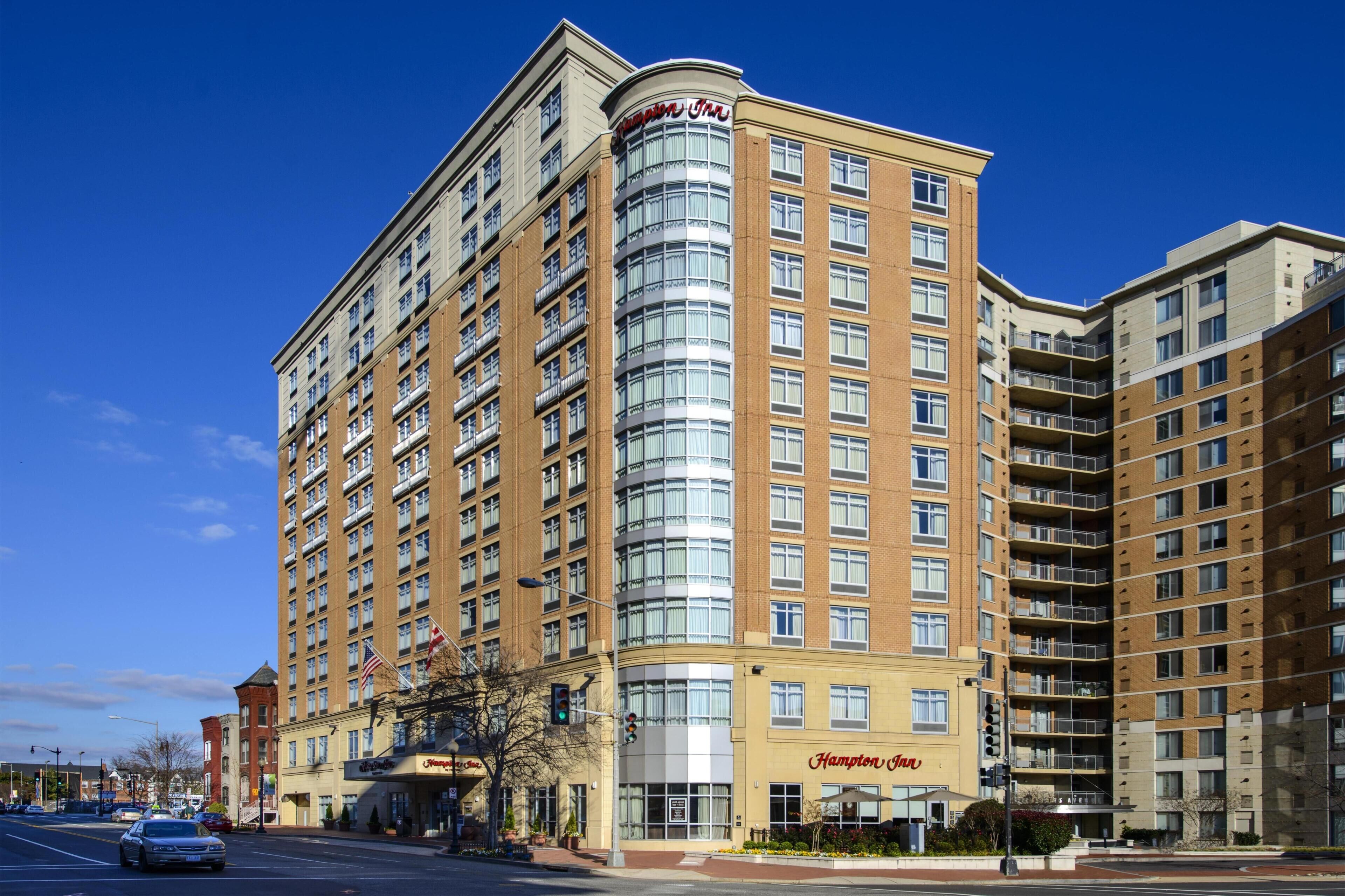 A multi-story hotel with a curved glass facade, a visible restaurant sign, and a clear blue sky.