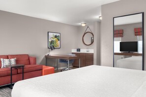 A hotel room with a bed, a desk, a chair, a sofa, a television, and a bathroom mirror. - Hampton Inn & Suites Fresno (Fresno)