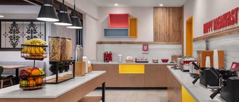 A modern breakfast area with a central island, seating, and a variety of food and drink dispensers.