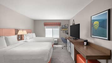 A hotel room with two beds, a desk, a TV, and a coffee machine.