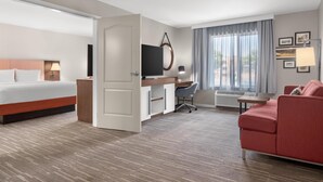 A hotel room with a bed, desk, office chair, sofa, and large windows with curtains. - Hampton Inn & Suites Fresno (Fresno)