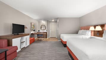 A hotel room with a bed, a desk with a computer, a TV, and a red chair.