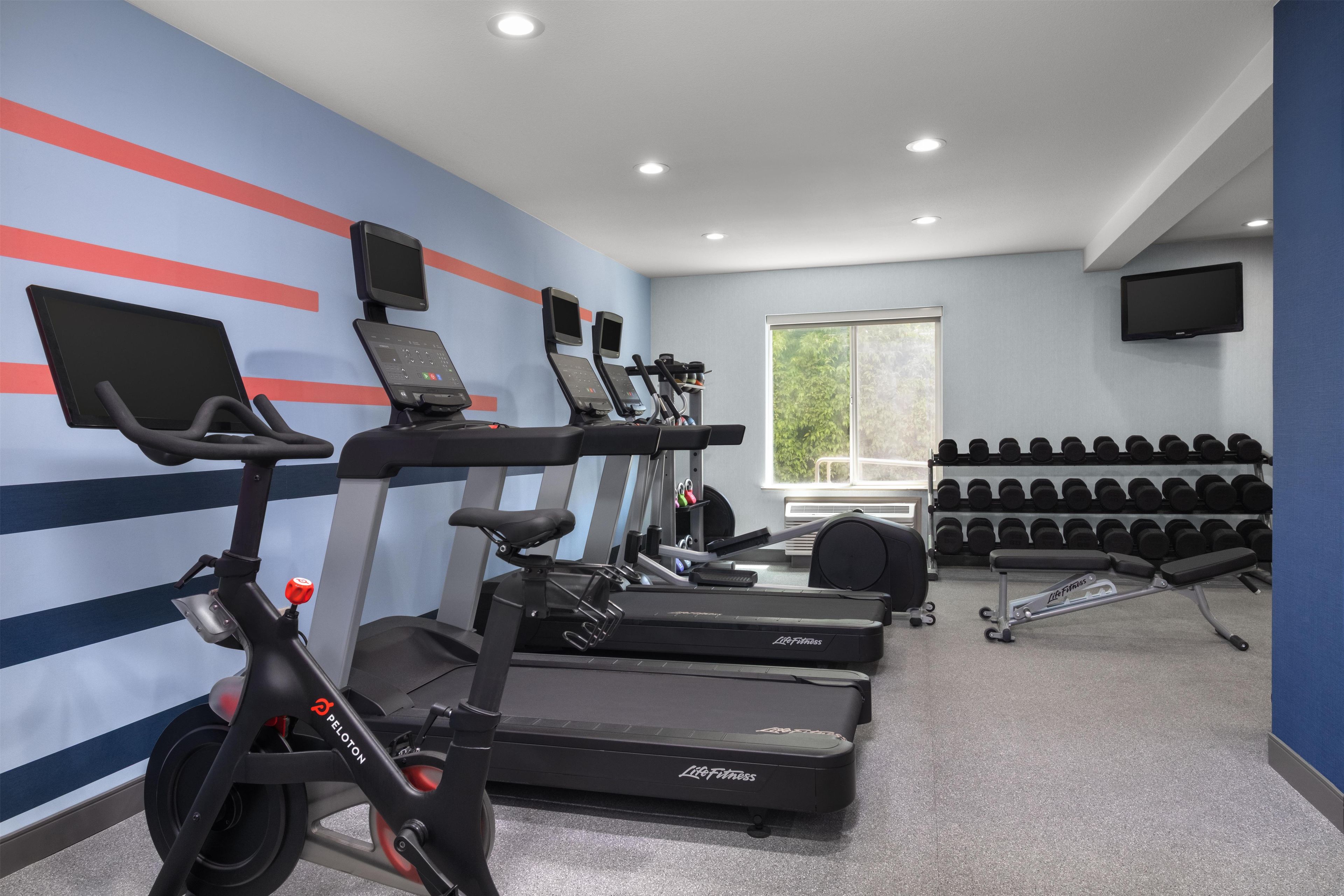 A gym with treadmills, an elliptical, and a rowing machine. There are dumbbells and a TV on the wall.