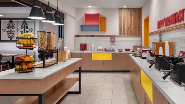 A modern kitchen with a breakfast bar, fruit baskets, and a 'Happy Breakfast' sign. - Hampton Inn & Suites Fresno (Fresno)