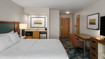 A hotel room with a large bed, a desk with a chair, a microwave, a coffee maker, and a framed picture on the wall.