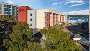 A hotel with a red and white facade, a marina with boats, and a clear blue sky. - Hampton Inn & Suites Bremerton (Bremerton)
