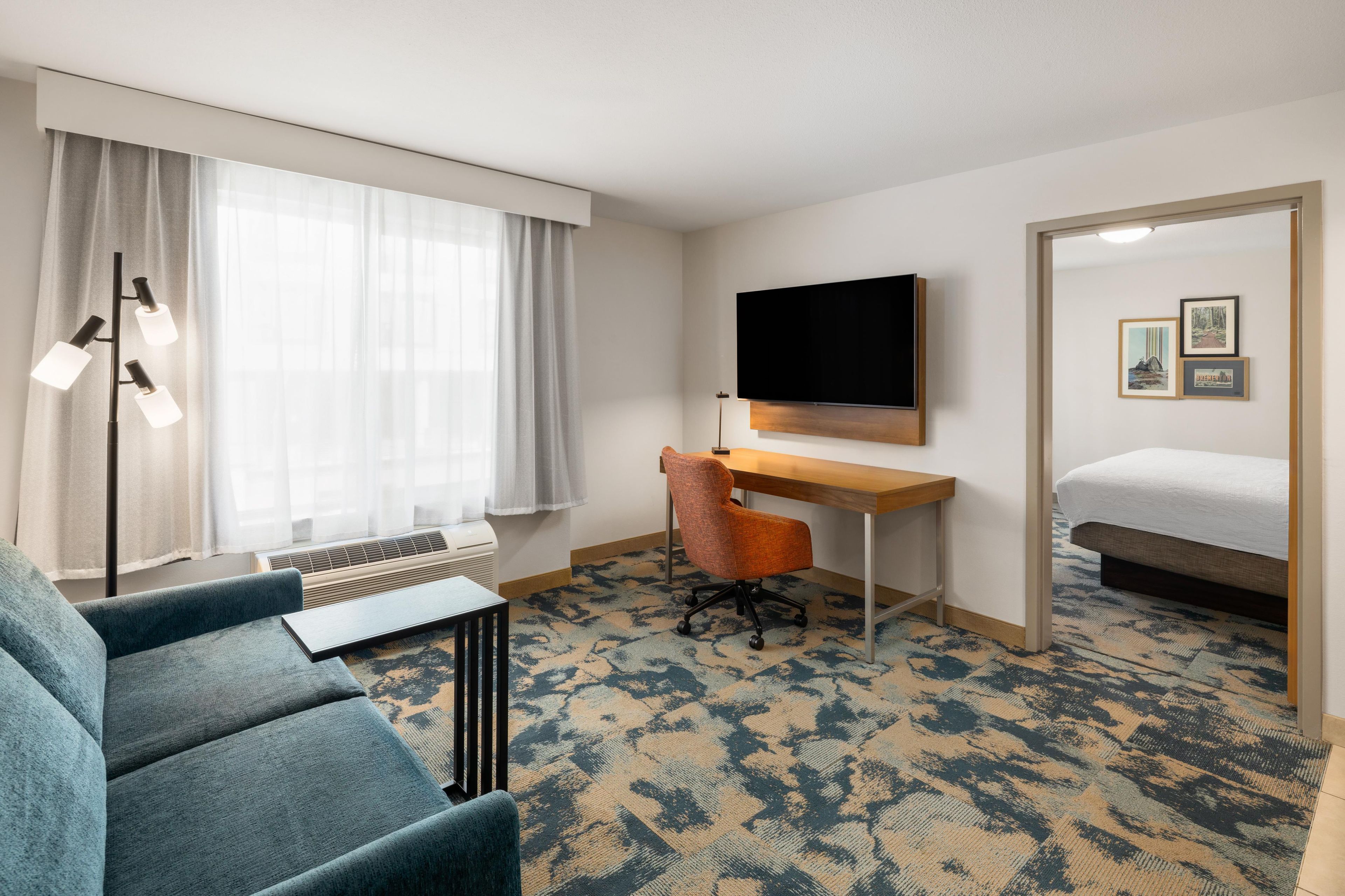 A hotel room with a bed, a desk, a chair, a television, and a window with curtains.