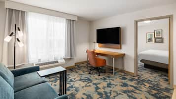 A hotel room with a bed, a desk, a chair, a television, and a window with curtains.