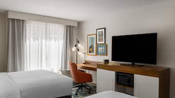 A hotel room with two beds, a desk with a flat-screen TV, a chair, and artwork on the wall.