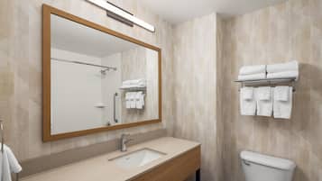 A bathroom with a wooden vanity, a sink, a mirror, a toilet, and a towel rack with towels.