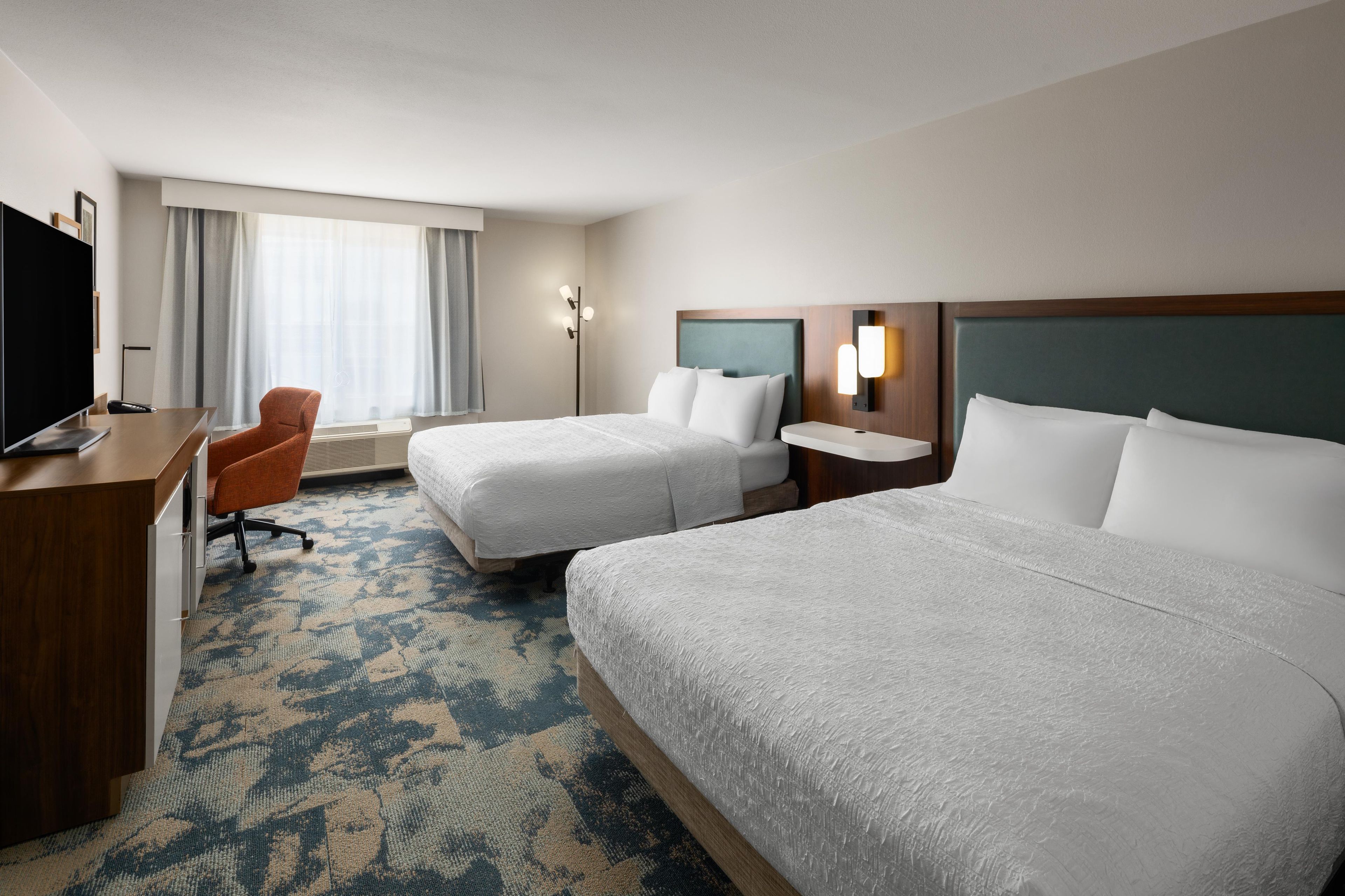 Une chambre d’hôtel avec deux lits, un bureau avec une télévision et une chaise.