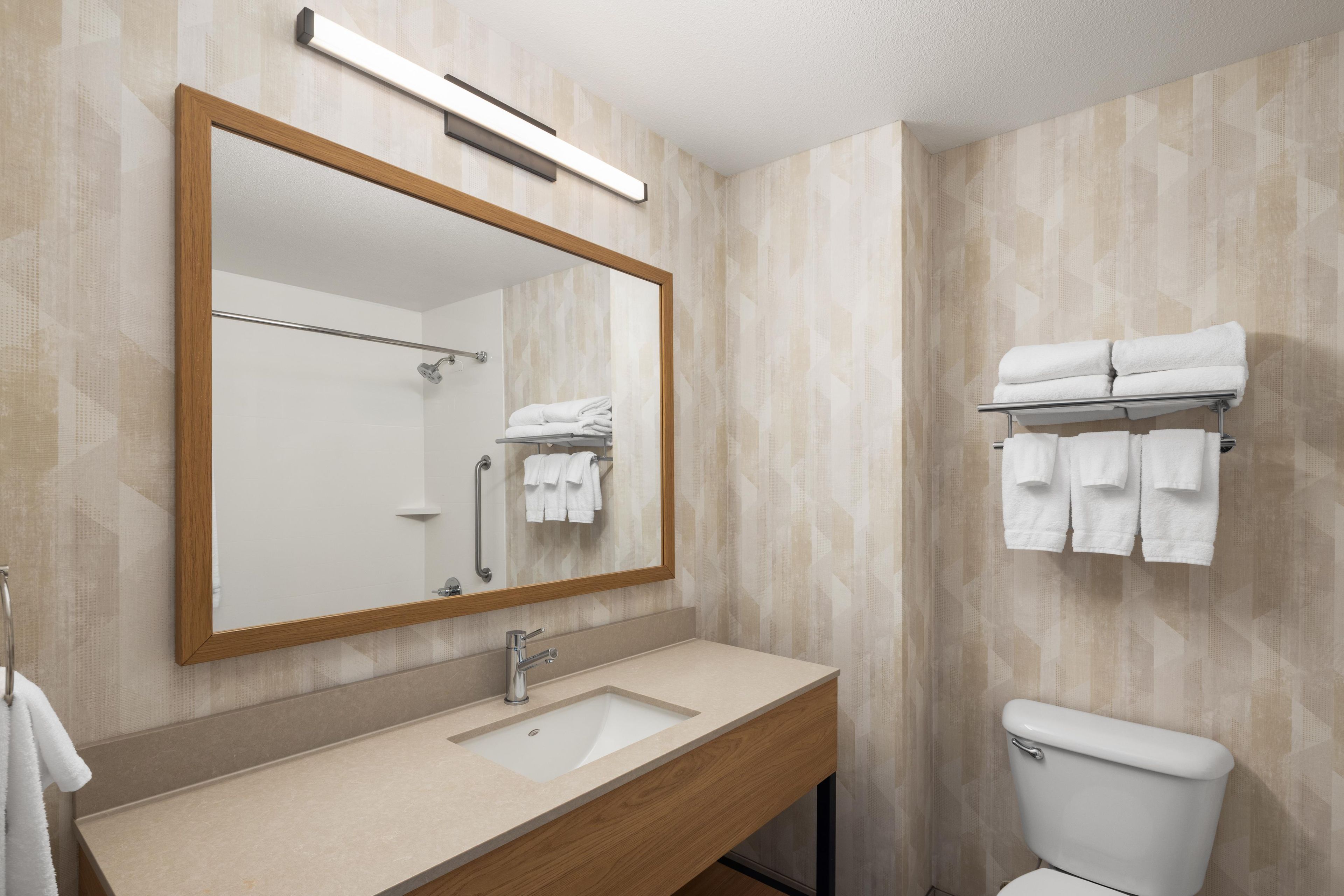 A bathroom with a wooden vanity, a sink, a mirror, a toilet, and a towel rack with towels.