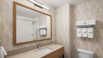 A bathroom with a wooden vanity, a sink, a mirror, a toilet, and a towel rack with towels.