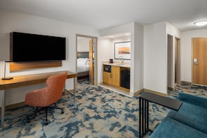 A hotel room with a bed, a desk, a television, a kitchenette, and a seating area.
