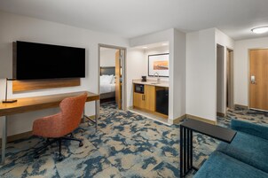 Habitación de hotel con cama, escritorio, televisión, kitchenette y zona de estar.