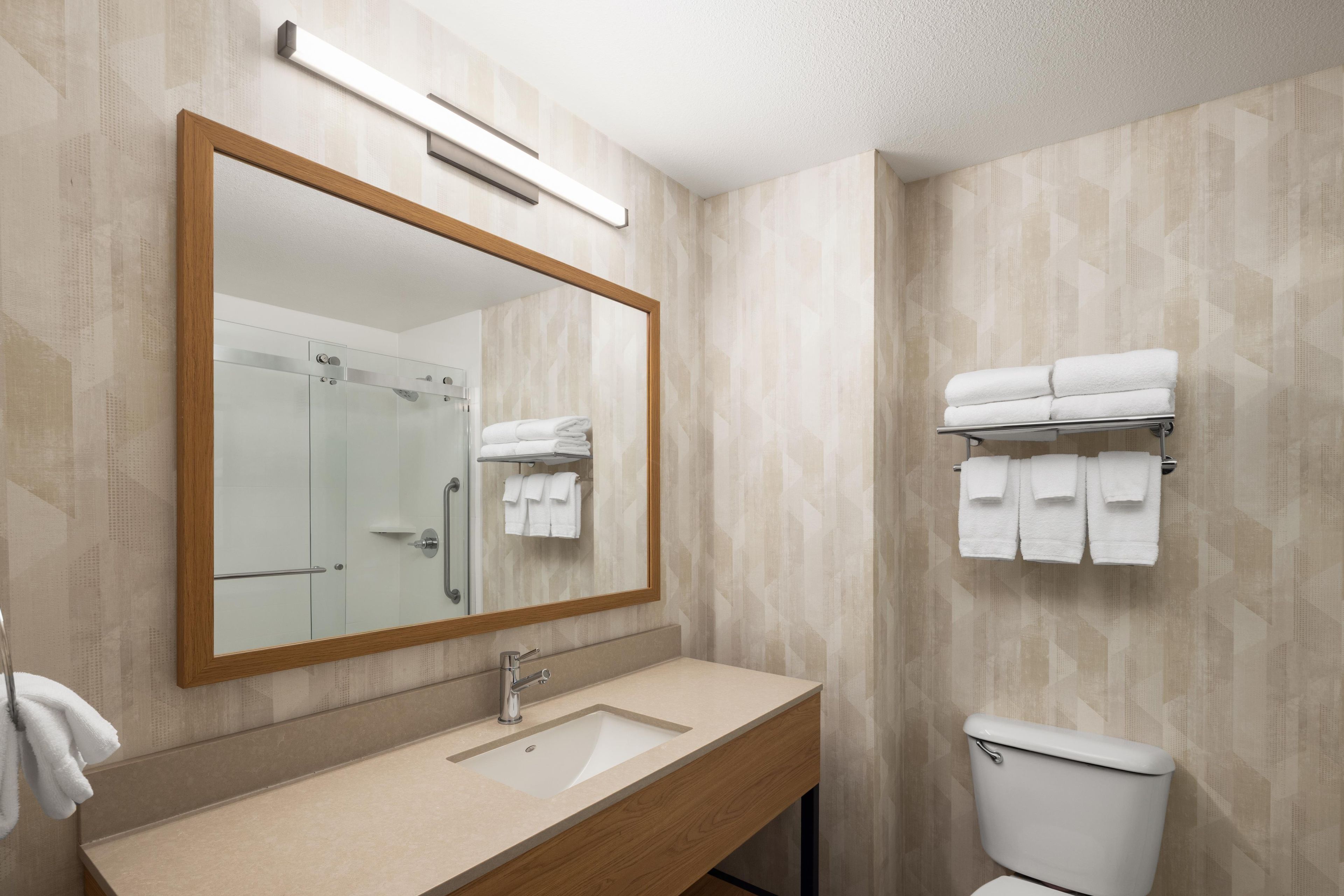 Een badkamer met een houten wastafelmeubel, een wastafel, een spiegel, een douchecabine van glas en een toilet.