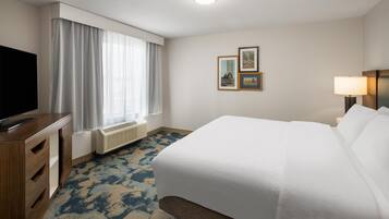 A hotel room with a bed, a television, a window with curtains, a radiator, a carpet, and two framed pictures on the wall.