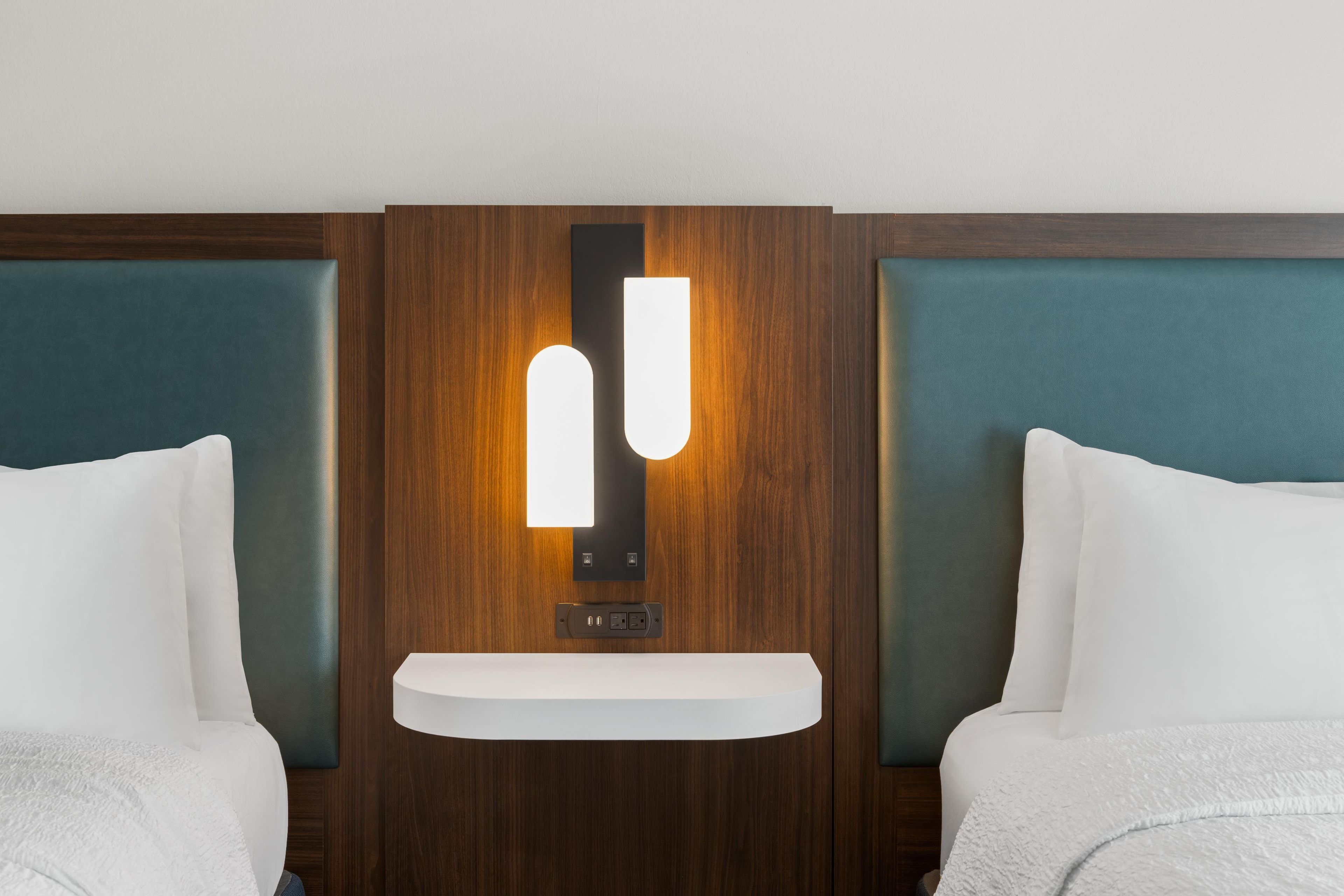Une chambre d’hôtel avec une tête de lit en bois, une table de chevet et deux oreillers blancs.