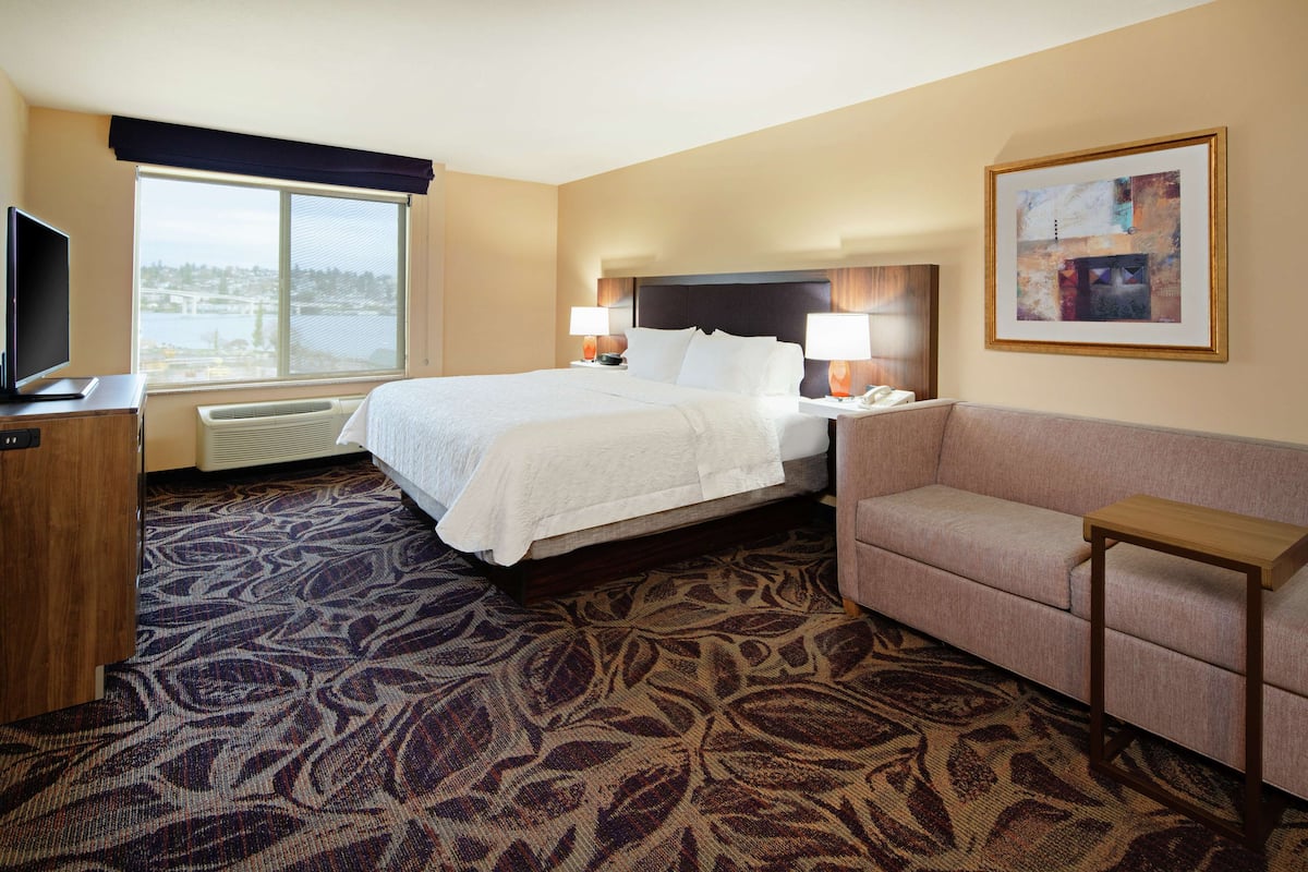 A hotel room with a large bed, a sofa, a television, and a large window with a view.