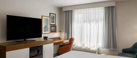 A hotel room with a large bed, a flat-screen TV, a desk with a chair, and a window with curtains.