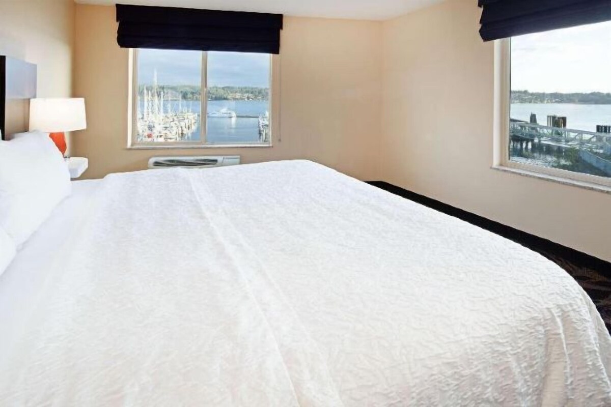 Une chambre d’hôtel avec un grand lit, une fenêtre donnant sur un plan d’eau et une table de chevet avec une lampe.
